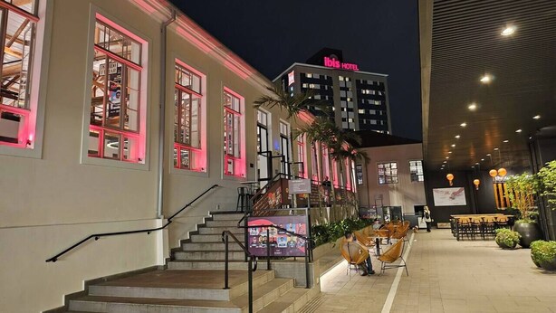 Entrada de un hotel con una escalera que lleva al vestíbulo, un área de estar al aire libre y un edificio moderno al fondo.