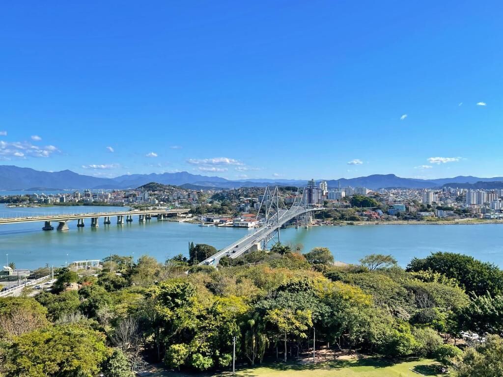 Un paisaje urbano con un puente destacado sobre un río, rodeado de vegetación y montañas al lejano.