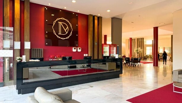A modern hotel lobby with a reception desk, seating area, and a large logo on the wall. - HOTEL DUNAMYS (Londrina)