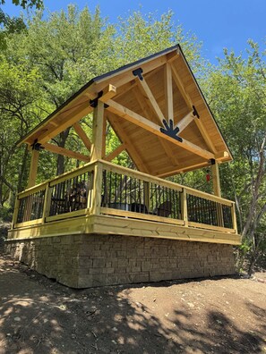 Un gazebo in legno su base di pietra, immerso nel verde.