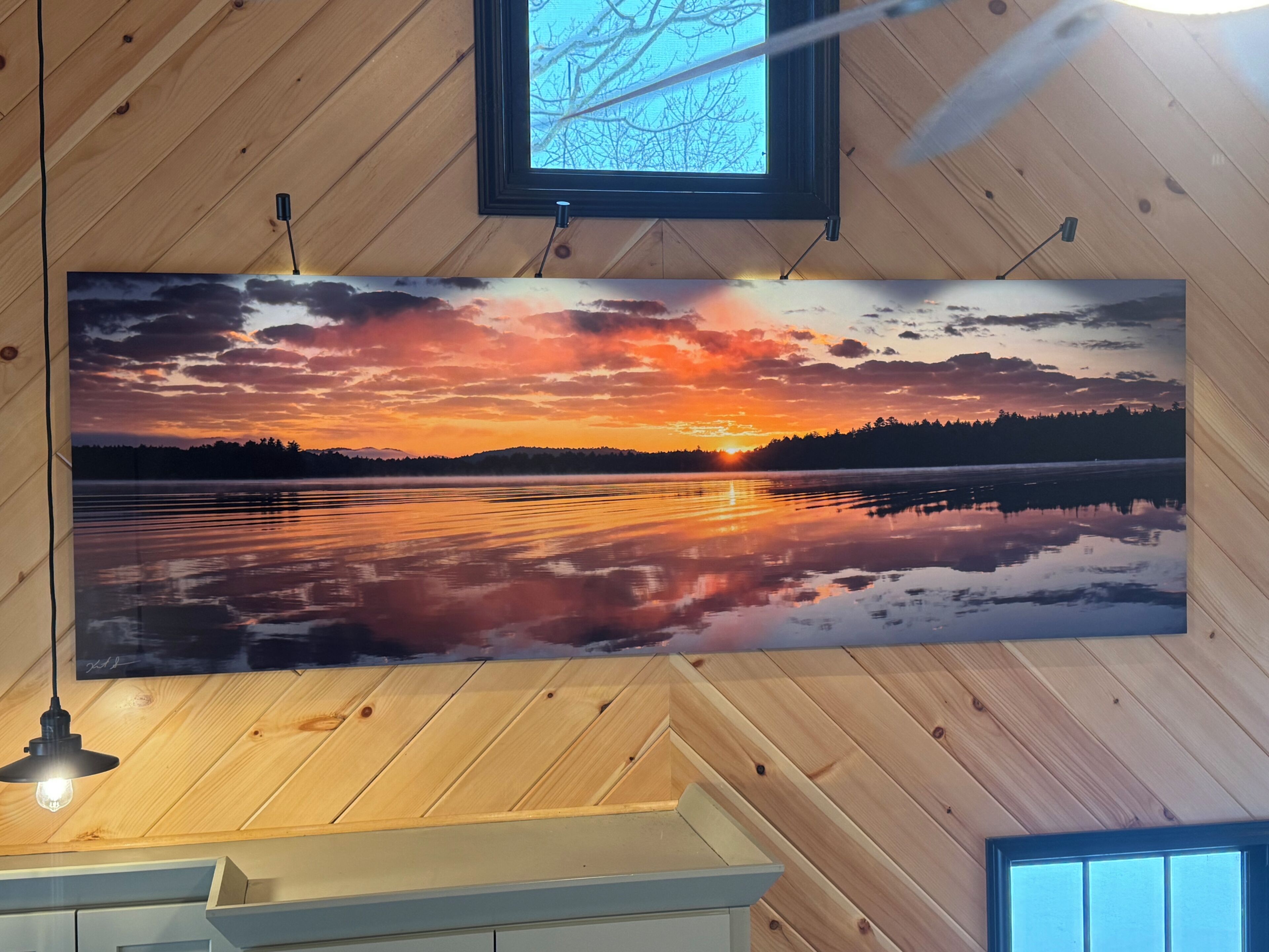 Eine Panorama-Wandmalerei zeigt einen Sonnenuntergang über einem See, eine Holzbalkendecke und ein kleines Fenster.