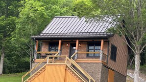 A cabin with a wooden staircase leading to a porch, surrounded by trees.