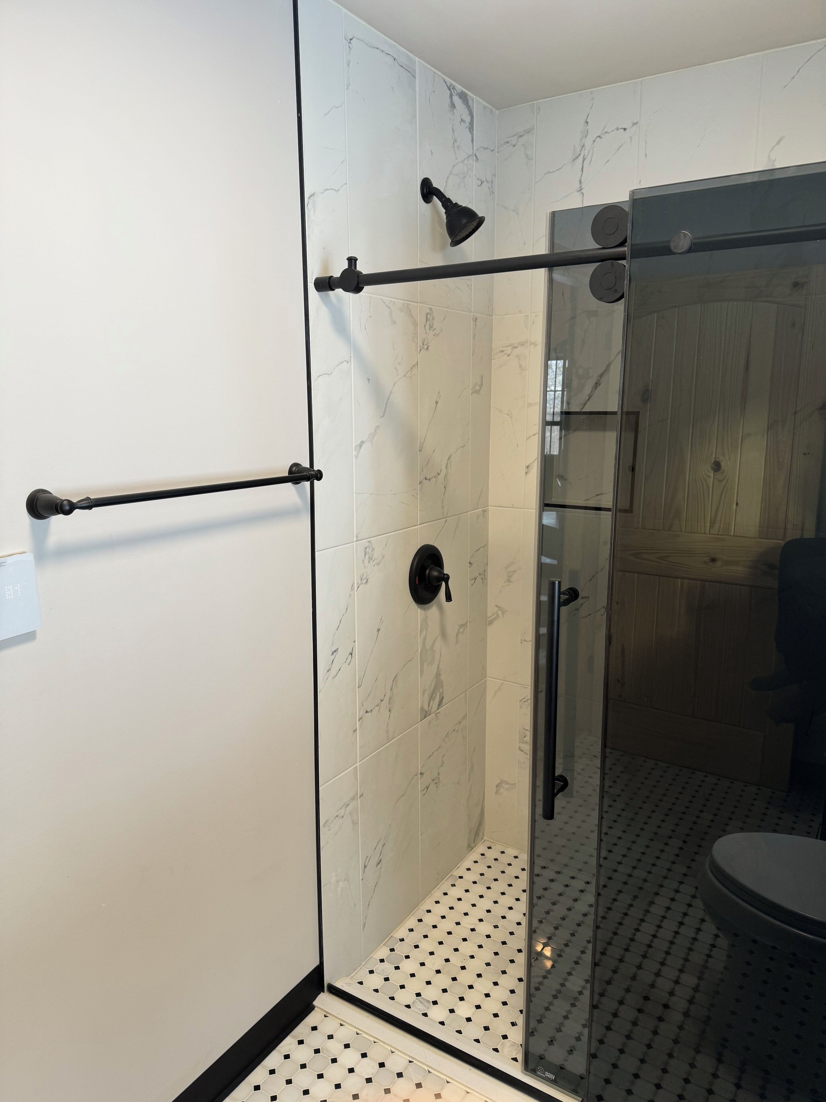 Een moderne badkamer met een douchecabine van glas, marmeren tegels en een wandpaneel van hout.