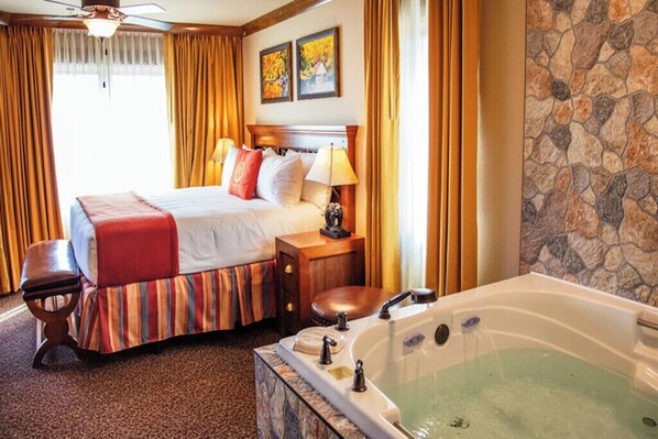 Habitación de hotel con cama, banco, mesita de noche, lámpara y bañera.