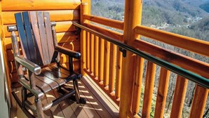 A wooden deck with a wooden chair and a railing overlooking a mountainous landscape. - Relax in Gatlinburg w/cool mountain views, FUN activities for all in the family! (Gatlinburg)