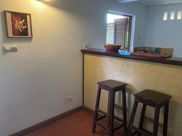 A small kitchen with a wooden countertop, two stools, a window with blinds, and a framed picture on the wall.