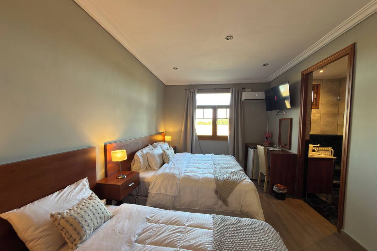 A hotel room with two beds, a desk, a TV, and a large window.
