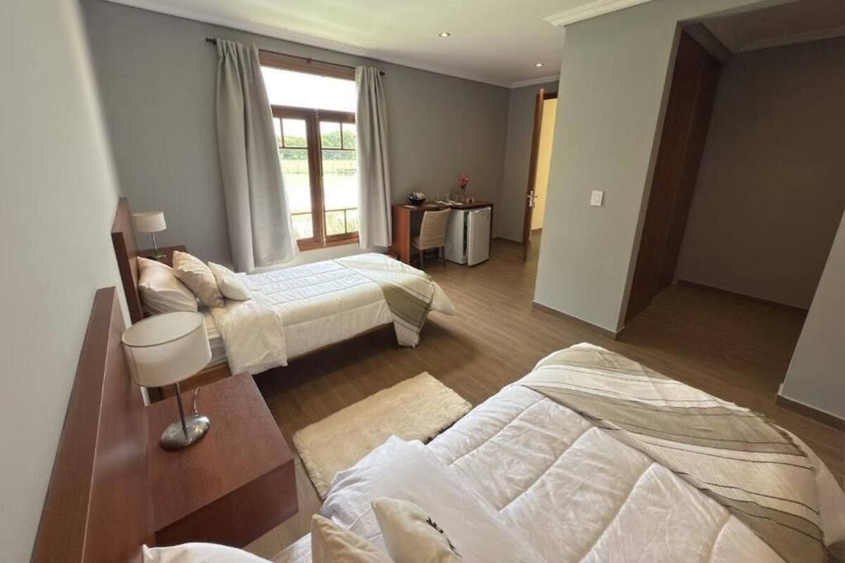 A bedroom with two beds, a desk, and a window with curtains.