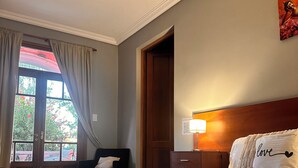 A hotel room with a large bed, a nightstand, a lamp, a window with curtains, and a door. - ESTANCIA LA ROSADITA (San Andres de Giles)