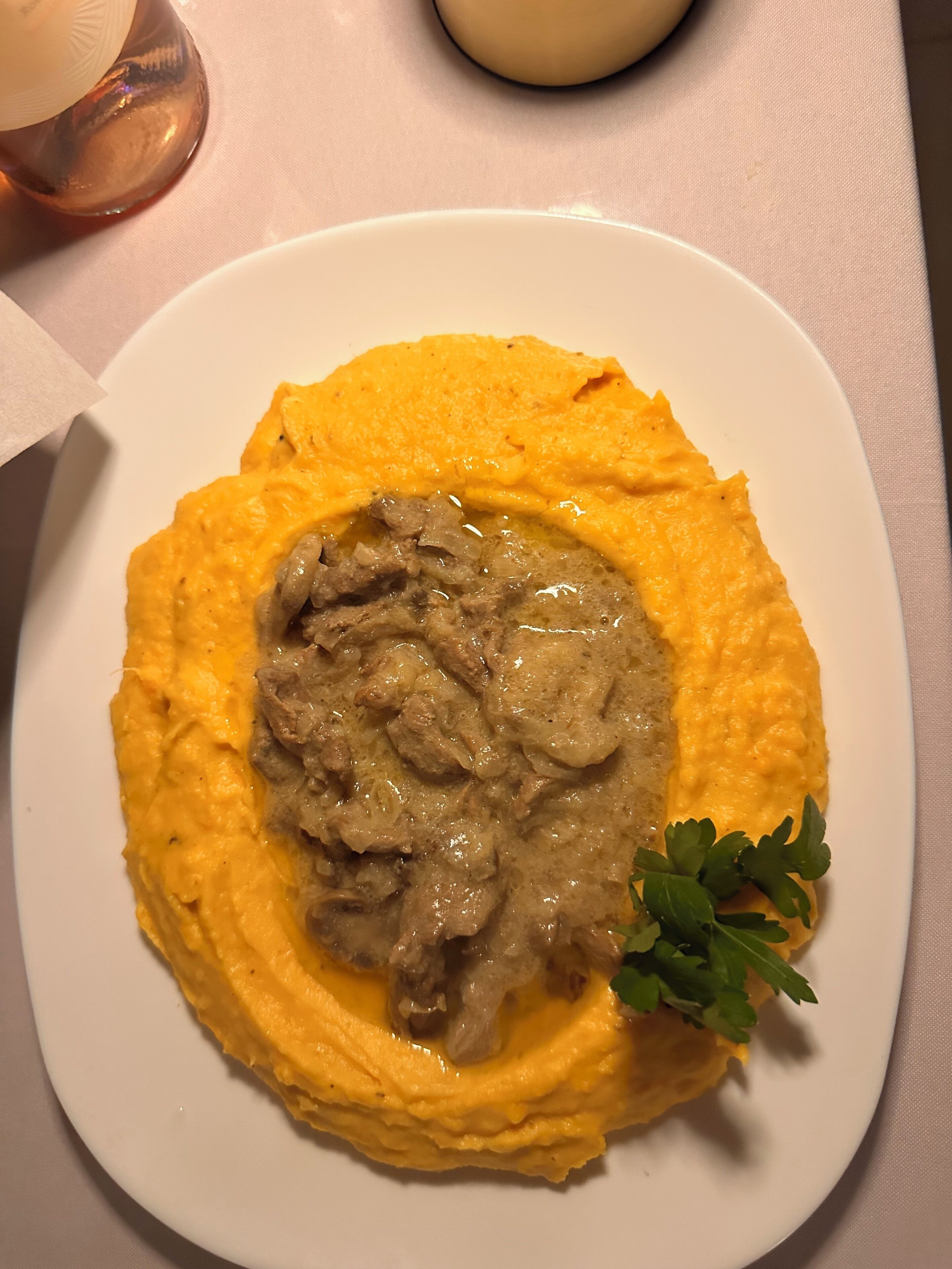 Un plato de comida con una base cremosa y un guiso de carne, adornado con perejil, sobre un plato blanco.