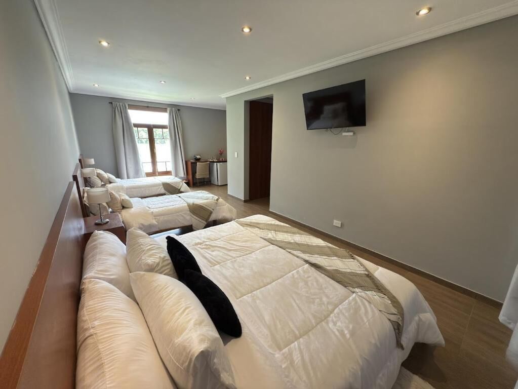 Habitación de hotel con una cama grande, un televisor en la pared y una ventana con cortinas.