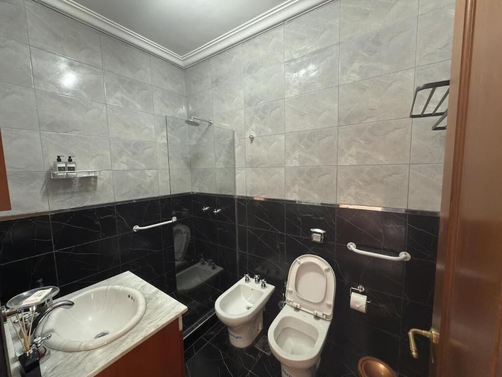 Un baño con un lavabo blanco, dos bidés, un inodoro y una ducha.
