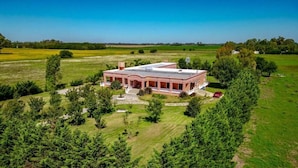 A large, single-story house with a flat roof, surrounded by dense trees and open fields. - ESTANCIA LA ROSADITA (San Andres de Giles)