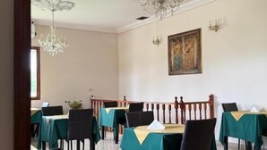 A dining area with tables set for six, each with a green tablecloth and black chairs. There are two chandeliers hanging from the ceiling. - ESTANCIA LA ROSADITA (San Andres de Giles)