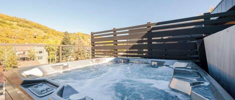 Un bain à remous avec une terrasse en bois et une vue sur une colline.