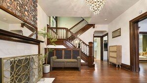 A spacious living area with a wooden staircase, a sofa, a decorative metal screen, and a chandelier. - Historic Gem | Soaking Tub • Fire Pit • EV Charger (Pittsburgh)
