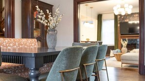 A dining area with a dark wood table, two upholstered chairs with metal legs, a vase with flowers, and a large chandelier. - Historic Gem | Soaking Tub • Fire Pit • EV Charger (Pittsburgh)