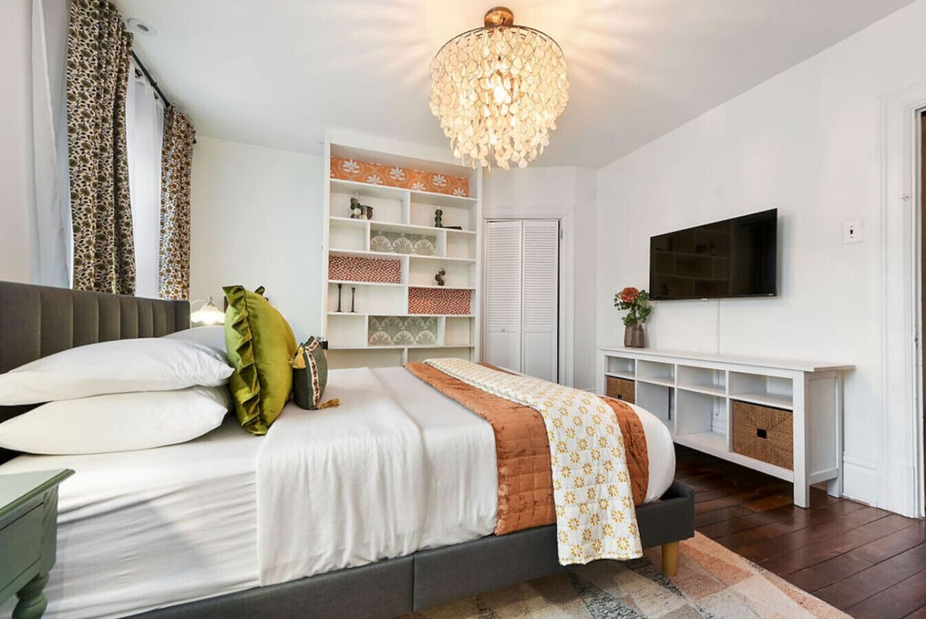 A bedroom with a bed, a TV, a chandelier, and a built-in shelf unit.