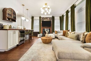 Ein geräumiges Wohnzimmer mit einer großen Couch, einem Couchtisch und einem Kamin. Es gibt eine Küchenzeile mit einer Bar und Stühlen.
