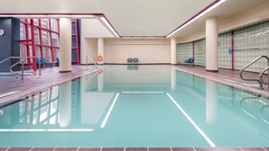 Piscina interna com água cristalina, rodeada por paredes revestidas e teto com iluminação embutida.
