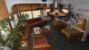 A cozy restaurant with wooden furniture, a large dining table, and hanging lights. - Sweet Pop (Santorini)