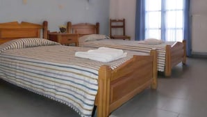 A room with three wooden beds, each with striped bedding. There are two wall-mounted lamps, a chair, and a small table. - Sweet Pop (Santorini)