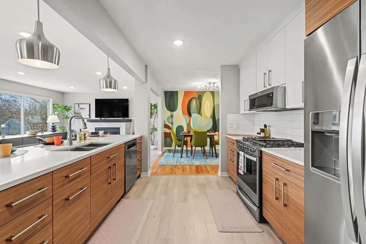 A modern kitchen with stainless steel appliances, wooden cabinets, and a large window overlooking the outdoors.