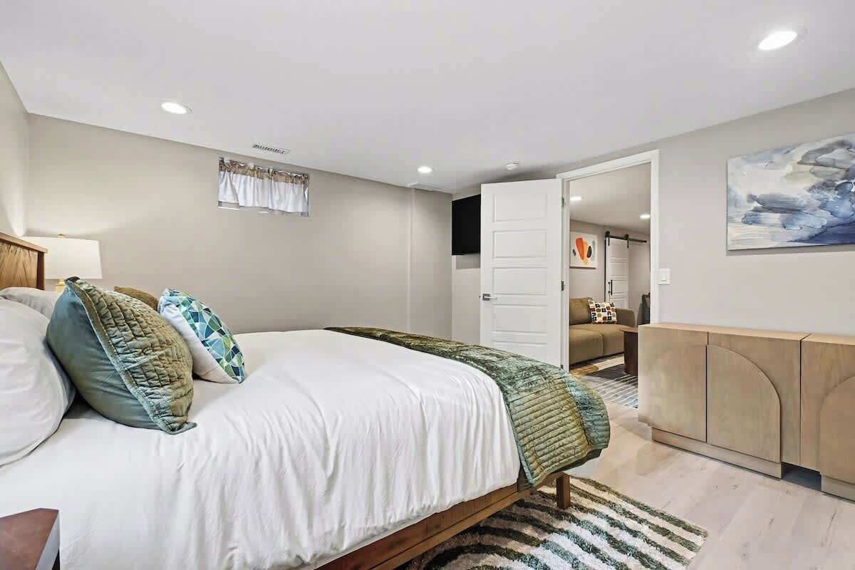 A modern bedroom with a large bed, a wooden headboard, a bedside table, and a wall-mounted TV.