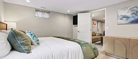 A modern bedroom with a large bed, a wooden headboard, a bedside table, and a wall-mounted TV.