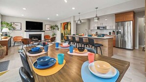 Een moderne keuken met roestvrijstalen apparatuur, een eethoek met kleurrijke kommen en borden, en een centraal kookeiland met barkrukken.