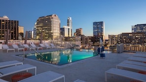 Ein Pool auf dem Dach mit Liegestühlen und einer Stadtansicht im Hintergrund.