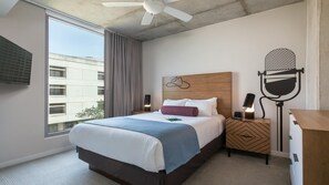 Ein Hotelzimmer mit Bett, Deckenventilator, Wand-Fernseher und Blick auf das äußere Gebäude.