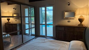 Un dormitorio con una cama, un aparador de madera, un espejo y una puerta corrediza de vidrio que da a una zona de piscina.