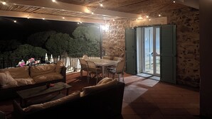 Un patio al aire libre con una mesa y sillas, un sofá y una silla de mimbre. Se aprecia una pared de piedra y un techo de madera.