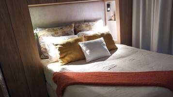 Un dormitorio con cabecera de madera, cama con colchón blanco y manta roja, y una ventana con cortinas.