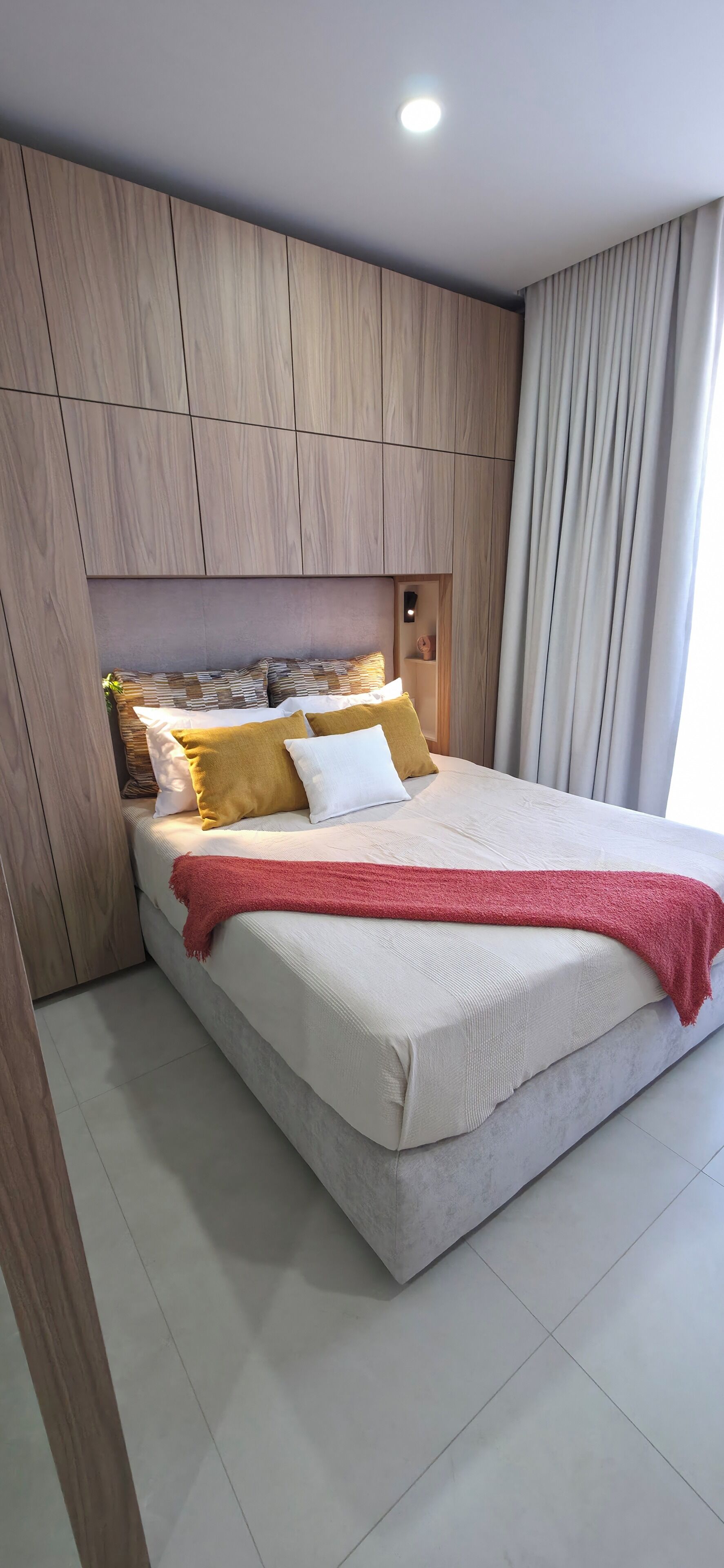 Een moderne slaapkamer met een bed, een houten hoofdbord en een rode plaid.