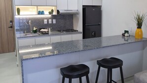 A modern kitchen with white cabinets, a black refrigerator, two bar stools, and pendant lights. - Ortega Living (Guadalajara)