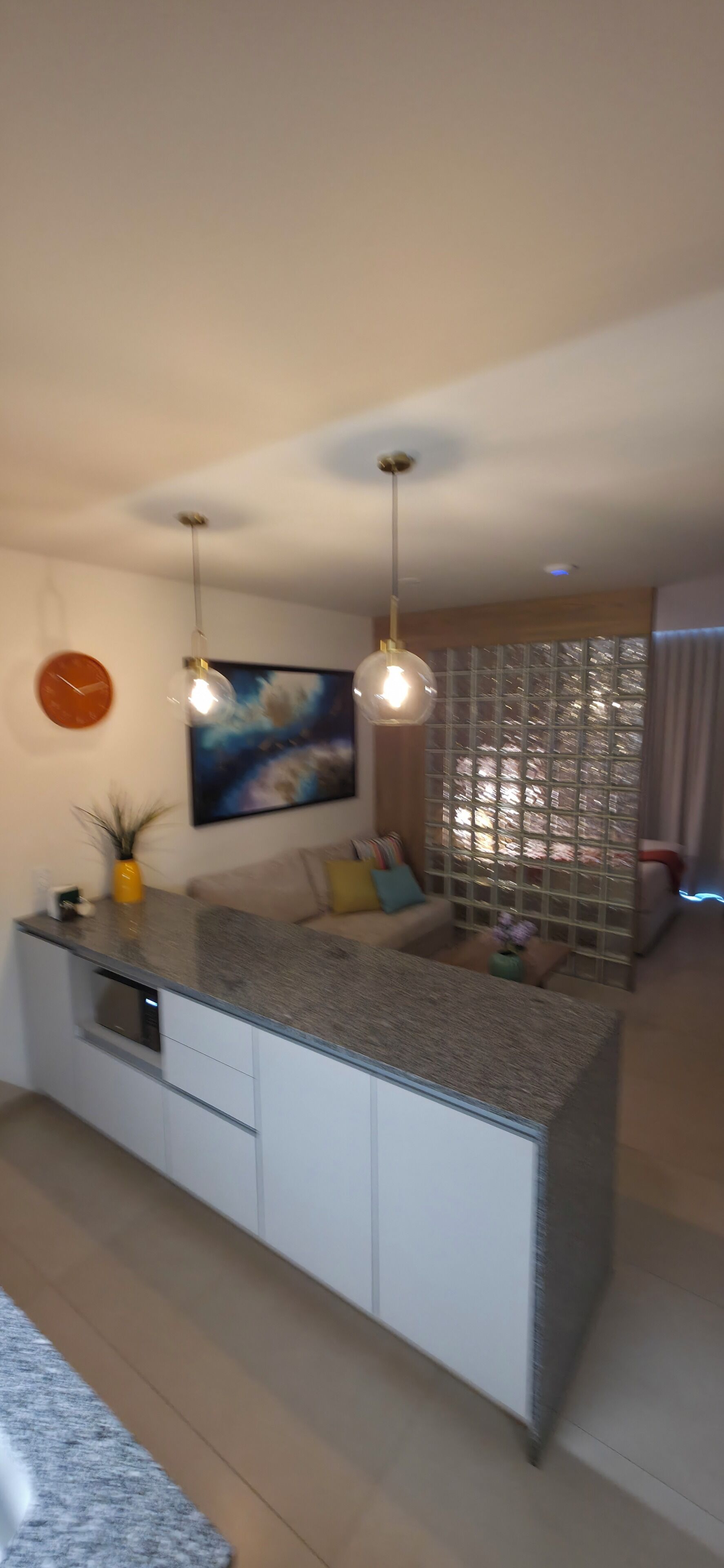 A modern kitchen with a central island, pendant lights, a clock, and a painting on the wall.
