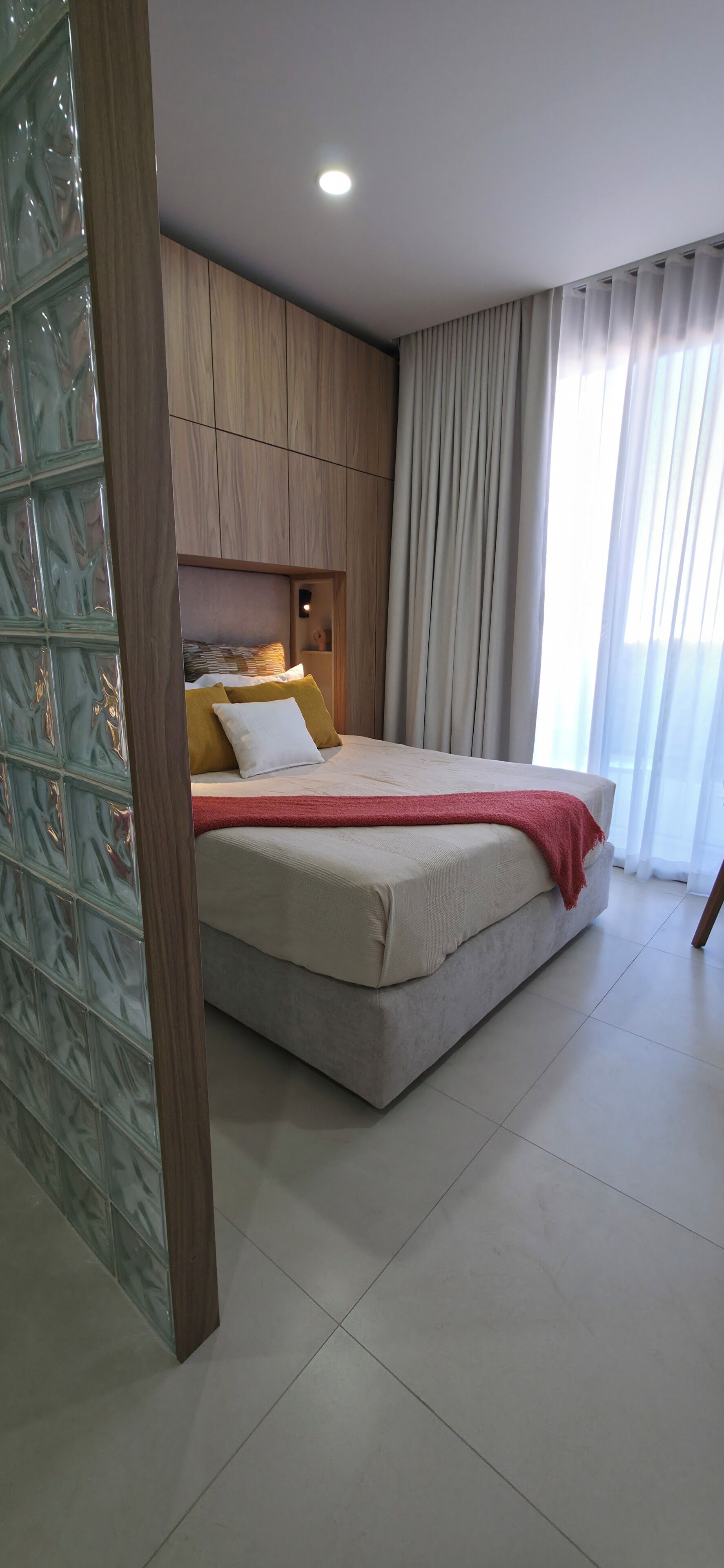Un dormitorio con cama, cabecera, mesita de noche y ventana con cortinas.