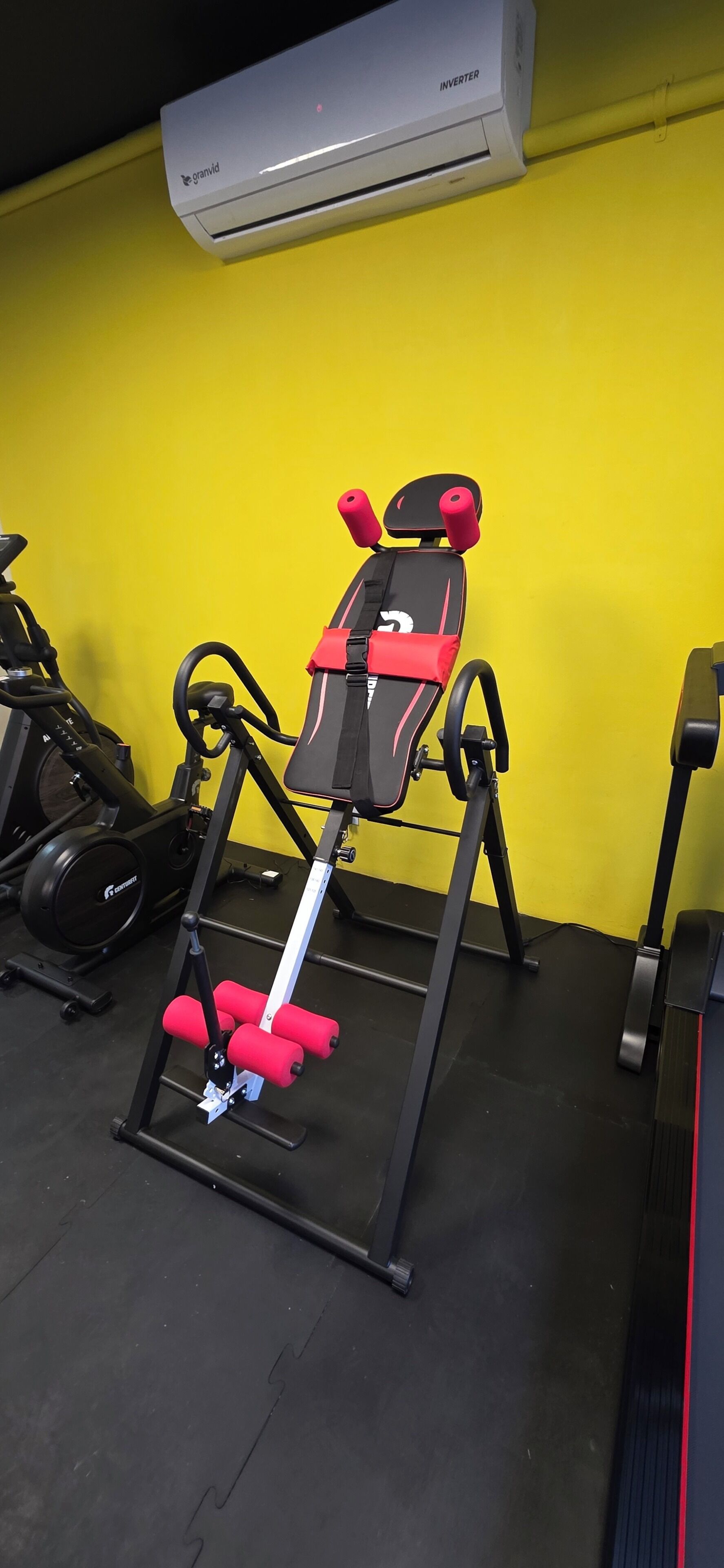 Un gimnasio con equipo de ejercicio, que incluye una bicicleta estática roja y negra y una máquina de pesas roja y negra.