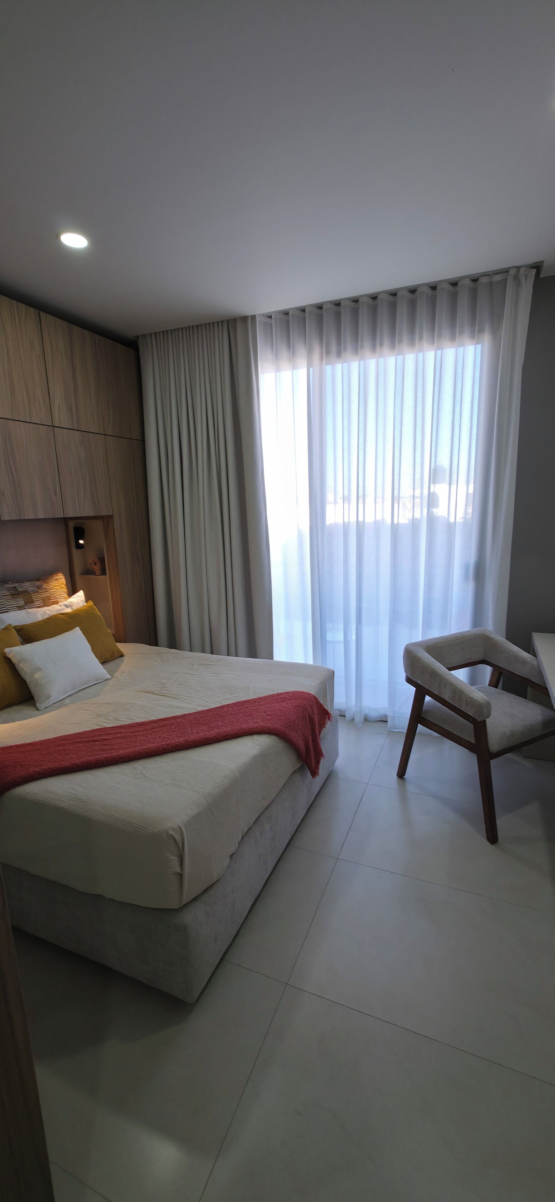 Une chambre à coucher avec un lit, une chaise, une fenêtre avec des rideaux et un luminaire au plafond.