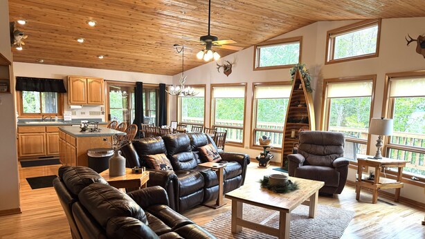 A spacious living area with a leather sofa, a wooden coffee table, and a dining table. There are large windows providing natural light and views of the outdoors. - Perfect 4-bedroom lakefront home on North Twin, great for a fun filled getaway! (Phelps)