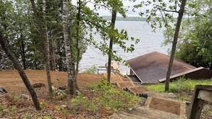 A wooden staircase leading to a dock by a lake, surrounded by trees and a small building with a sloped roof. - Perfect 4-bedroom lakefront home on North Twin, great for a fun filled getaway! (Phelps)