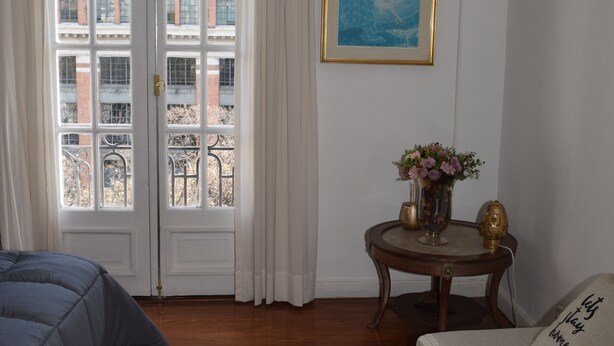 Ein Zimmer mit Holzboden, einem Bett, einem Sofa, einem Tisch mit einer Vase und einem gerahmten Bild an der Wand.