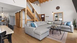 A spacious living area with a large gray sectional sofa, a wooden staircase, and a dining area with a wooden table and chairs. - Private Naples Retreat | Near Wineries | Hot Tub (Naples)