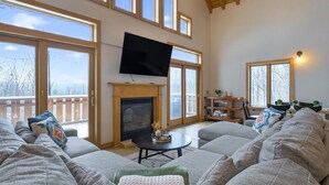 A spacious living room with a fireplace, large windows, and a flat-screen TV. - Private Naples Retreat | Near Wineries | Hot Tub (Naples)