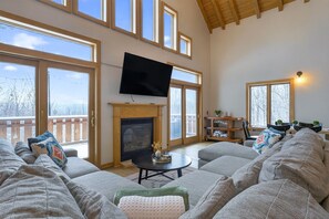 Un salón amplio con chimenea, ventanas grandes y un televisor de pantalla plana.