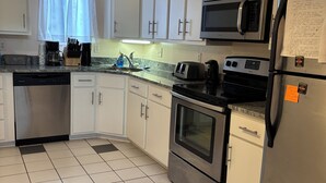 Een keuken met witte kastjes, een roestvrijstalen koelkast, een magnetron, een broodrooster en een vaatwasser.