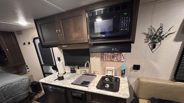 A compact RV kitchen with a microwave, stove, sink, and a small countertop area. - Cozy 1-bedroom camper in beautiful Manitowoc, walking distance to Lake Michigan (Manitowoc)