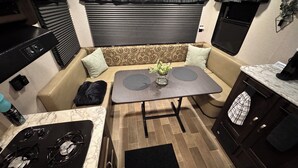 A compact kitchenette with a stove, a small table with a vase, and a sofa with cushions. - Cozy 1-bedroom camper in beautiful Manitowoc, walking distance to Lake Michigan (Manitowoc)